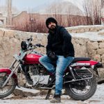 Man sitting on a red motorcycle in a snowy outdoor setting, India.