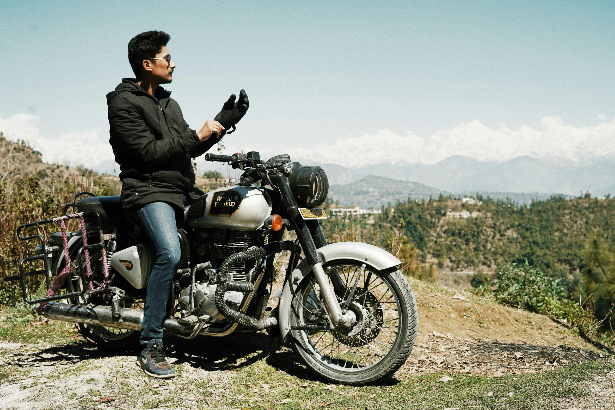 Man on a motorcycle enjoying a scenic mountain view under bright sunlight.